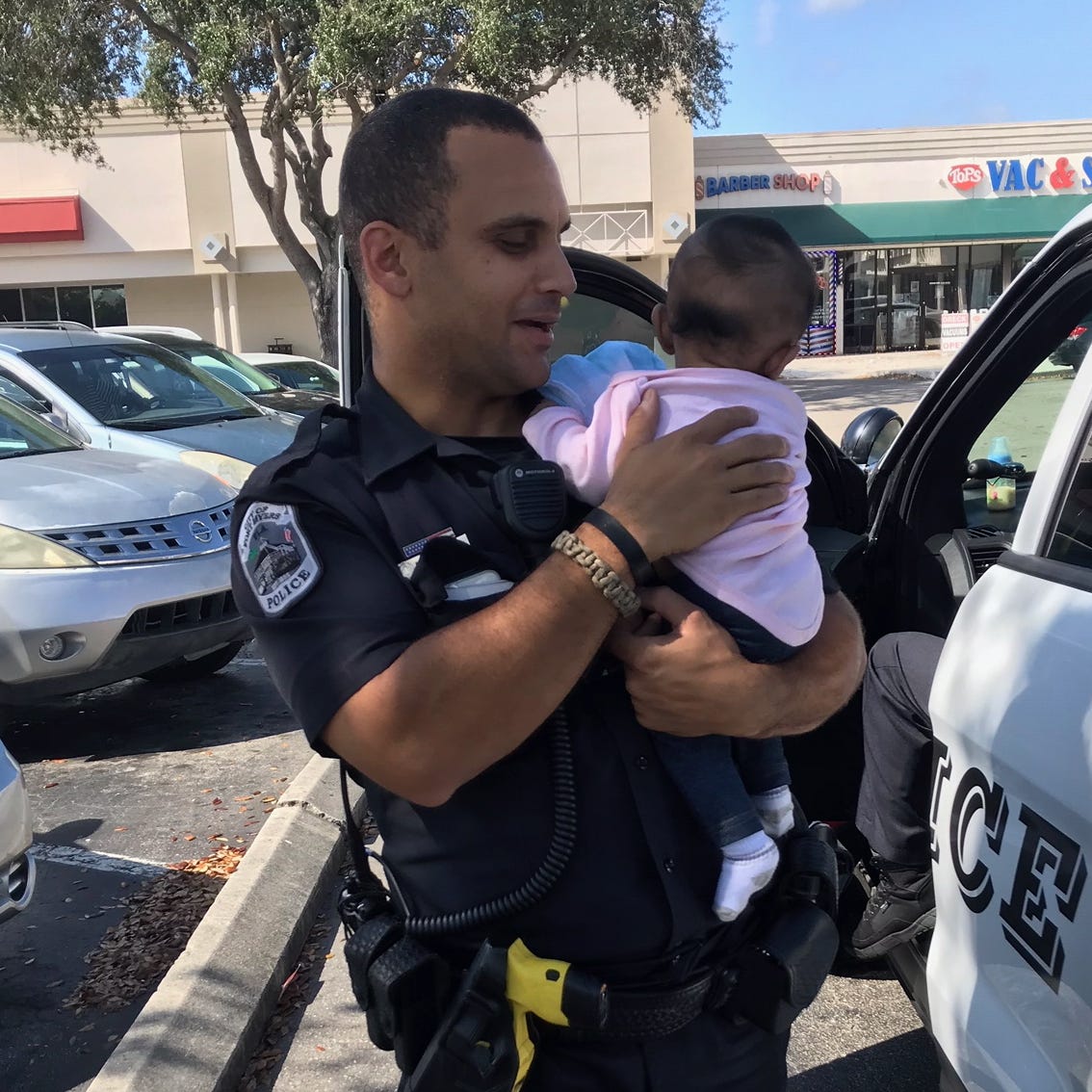 A Fort Myers police officer holds a 4-month-old infant left in a locked car by parents while they shopped at Dollar Tree in the Sam's Club Plaza, 5100 S. Cleveland Ave., about 10 a.m. Thursday.