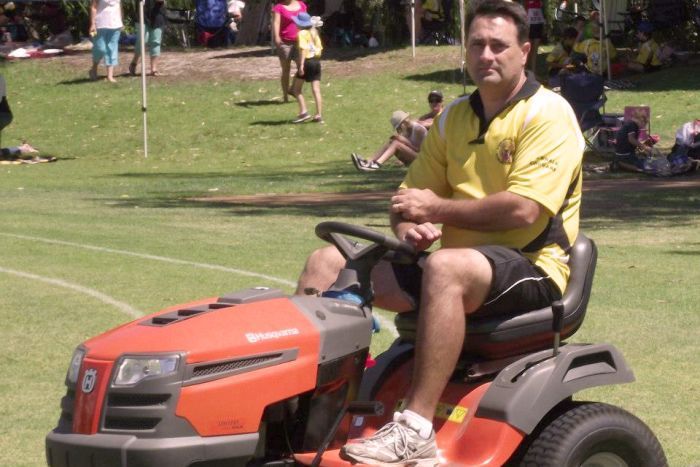 Bradley Robert Edwards sits on a red ride-on lawnmower on a grass oval in a yellow shirt.