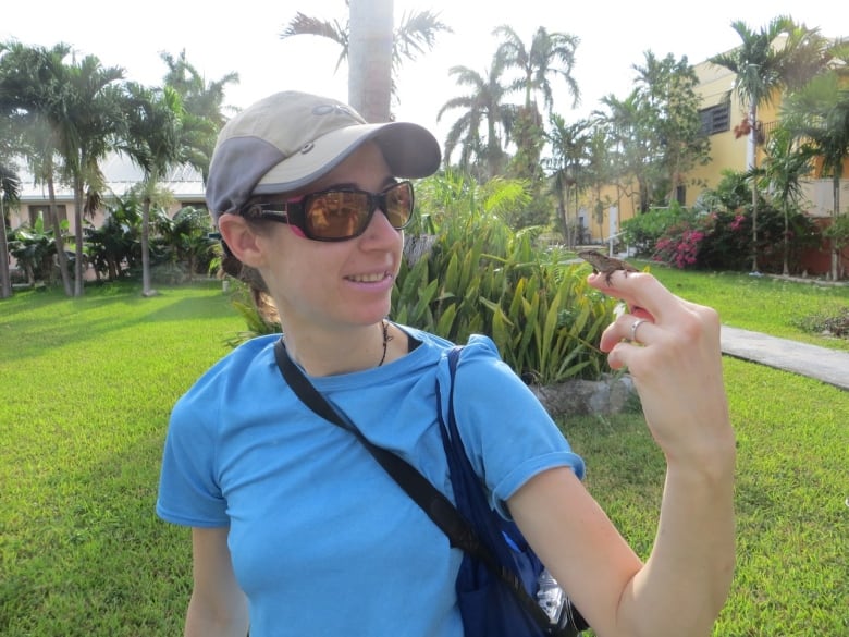  A woman with a ballcap and sunglasses holds a tiny lizard on her finger.