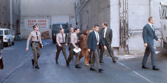 Charles Manson, accused leader of a hippie cult charged with the Tate-LaBianca murders, is heavily guarded as he leaves the Hall of Justice following arraignment Dec. 11.